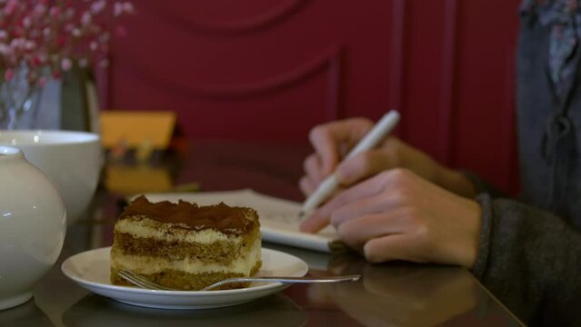 Girl artist draws in a cafe, in the foreground is a piece of tiramisu