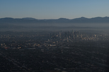 The hazy, polluted air obscures an aerial view from high above Los Angeles. The cityscape is mostly...