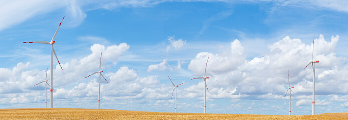 Large panorama of wind turbines with blue sky and white clouds in the background