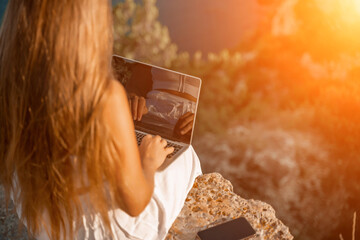Freelance happy woman typing on her laptop, enjoying the picturesque sea view, highlighting the idea of working remotely with a relaxed and pleasant atmosphere.
