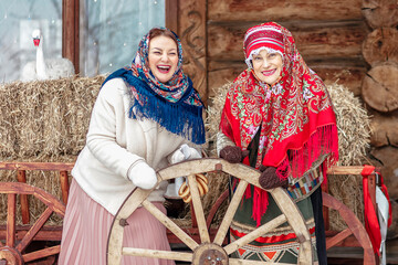 Two beautiful Slavic women in national traditional Slavic costumes on the roof of a wooden tower against the backdrop of a snow-covered city. Pancake day