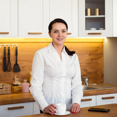 Portrait of smiling young woman with cup of coffee in kitchen at home