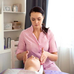 Masseur doing massage on the face of a young woman in a beauty salon