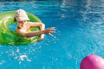 Little boy has a fun with pink ball on swimming pool.