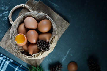 Fresh raw chicken eggs in the basket on dark background. one chicken egg broken