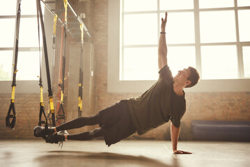 Making perfect body. Young athletic man exercising with suspension straps at gym