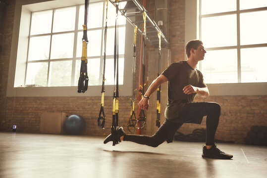 TRX Training. Young athletic man in sports clothing training legs with trx fitness straps in the gym