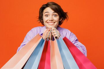 Young happy cool excited woman wearing purple shirt casual clothes hold in hand paper package bags after shopping isolated on plain orange color background studio. Black Friday sale buy day concept.