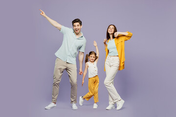 Full body young cheerful happy parents mom dad with child kid daughter girl 6 years old wearing blue yellow casual clothes raise up hands dance isolated on plain purple background. Family day concept.
