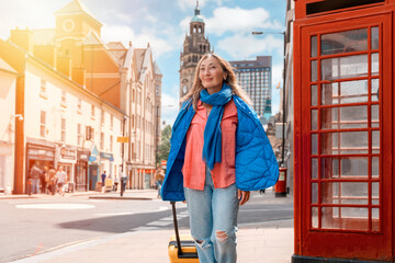 Asian woman in blue jacket with yellow suitcase  walking around English city. Lifestyle local tourism and resting concepts