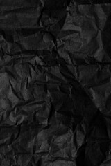 A sheet of black wrinkled paper. Texture of black crumpled paper. Dark paper background with chaotic bends.