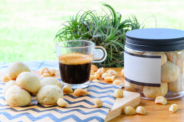 Macadamia nut and cookies in plastic box next to black coffee on wooden table in backyard