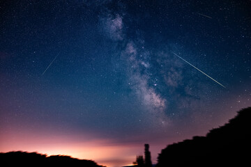 Milky way stars, shooting stars and countryside silhouettes photographed with wide angle lens.