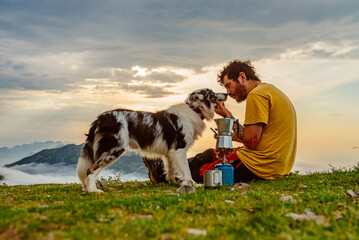 white man and young mountaineer sitting next to his border collie breed dog while preparing coffee...