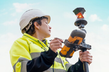 Close-up portrait of a woman site engineer surveyor working with theodolite total station EDM equipment on a building construction site outdoors