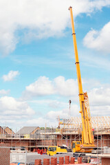 Fototapeta na wymiar Mobile crane at building site lifting joist for new house roof construction