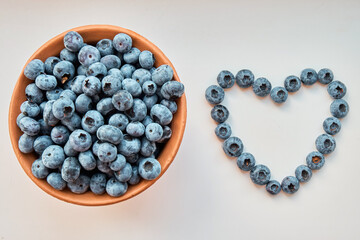 A heart lined with blueberries and a pitcher of blueberries on a white background. Berries, healthy food, healthy immunity. View from above