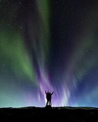 Two people silhouettes standing under the northern lights, aurora borealis in Iceland