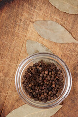 Peppercorns in glass bowl on wooden background with bay leaves. Seasoning mix, top view. 