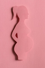 silhouette of pregnant woman on pink background, monochrome. waiting childbirth, reproductology, gynecology. happy duration of pregnancy. concept birth of child. Design cut out of paper. vertical