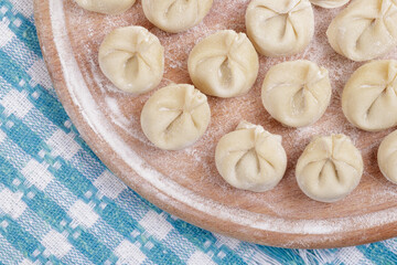 Homemade uncooked dumplings on a wooden board on the checkered tablecloth. Dumplings closeup. Top view