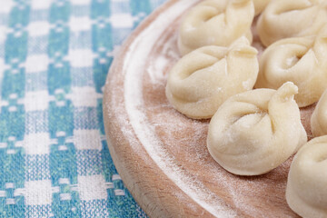 Homemade uncooked dumplings on a wooden board on the checkered tablecloth. Dumplings closeup.