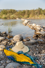 river bank with rounded stones, straw panama hat, water bottle and dress