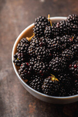 Blackberries in ceramic bowl on rustic wooden background. Selective focus. Shallow depth of field.