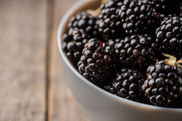 Blackberries in ceramic bowl on rustic wooden background. Selective focus. Shallow depth of field.