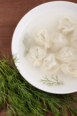 Bouillon with homemade pelmeni and fresh dill. Soup with dumplings and herbs. Top view.