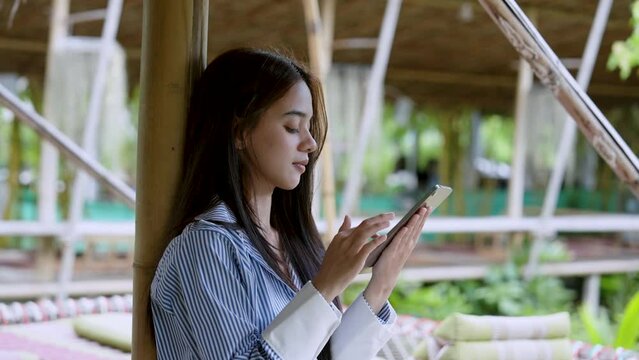 Beautiful Asian women hang out during long weekend, with good weather cool breeze, woman watching scrolling on tablet in hand, comfort being able come out play enjoy made her smile.