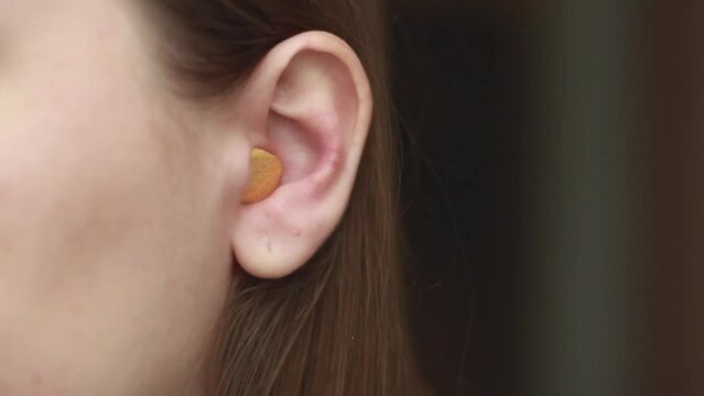 Woman inserting earplugs into her ear close-up