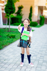 a first-grader girl with a backpack and a book in her hands at the school is reading a book or doing homework, the concept is back to school