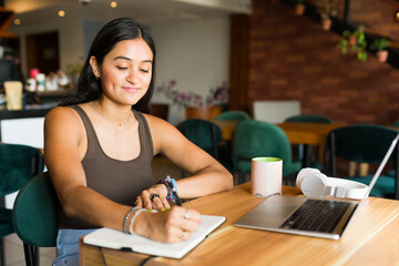 Happy young woman writing while doing freelance work