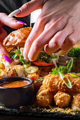 woman chef hands cooking fast food set on plate. burger, potato chips, french fries, chicken wings, fried cheese and more on table.