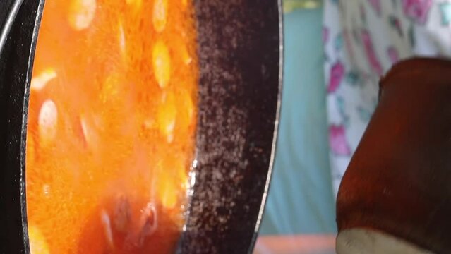 Solyanka soup on an open fire. The cook stirs the soup with a slotted spoon. vertical video.