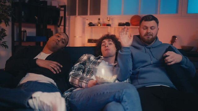 Three carefree male friends watching TV together, eating popcorn, guys night