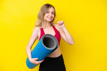 Young sport caucasian woman going to yoga classes while holding a mat isolated on yellow background proud and self-satisfied