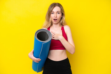 Young sport caucasian woman going to yoga classes while holding a mat isolated on yellow background surprised and shocked while looking right