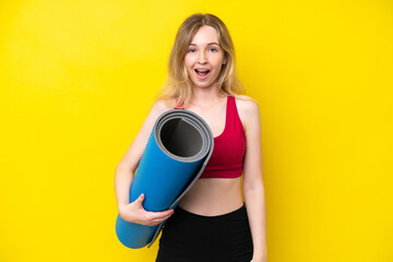 Young sport caucasian woman going to yoga classes while holding a mat isolated on yellow background with surprise facial expression