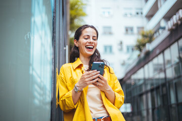 Smiling young woman with smart phone walking on the street, with copy space. Beautiful young woman...