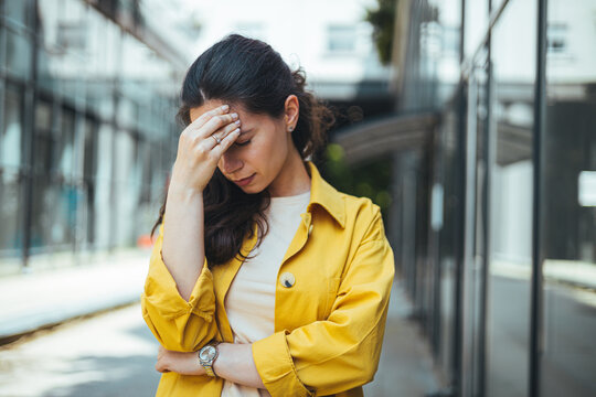 Portrait Of A Young Frustrated Girl Standing In The Crowd, Headache Or Anxiety Attack, City Life Problems. An Angry Frustrated Woman In The Middle Of The Busy City Traffic.