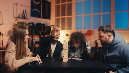 Group of young people playing jenga and drinking beer, leaning tower game