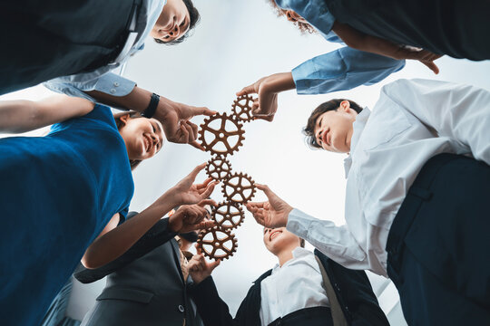 Below view office worker holding cog wheel as unity and teamwork in corporate workplace concept. Diverse colleague business people as symbol of visionary system teamwork for business success. Concord