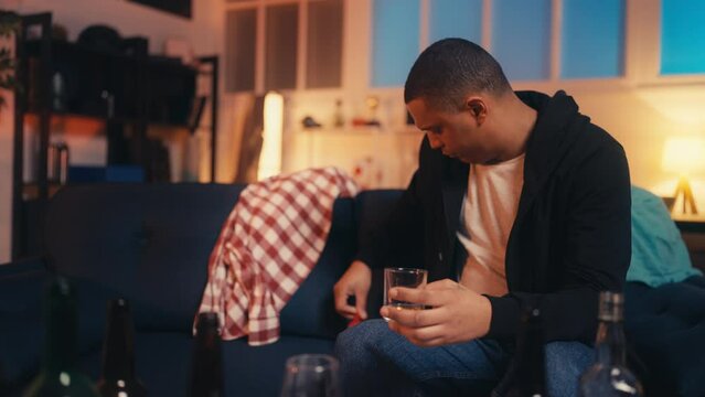 Funny African American man discovers red bra on sofa, party aftermath, hangover