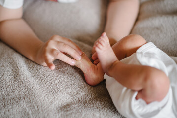 Baby sister's feet in brother's hands. Young child holding infant feet. Cute little baby lying on bed at home. Kid hold legs. Closeup. Tiny, bare feet of newborn baby girl or boy wrapped in hands.