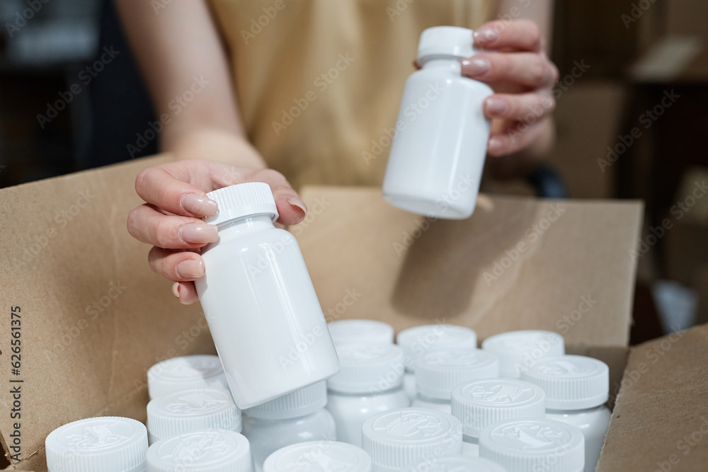 Wall mural closeup of unrecognizable young woman putting blank pill bottles in boxes at pharmaceutical factory 