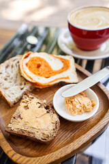A slice of bread with butter on a chopping board. Assorted sliced bread on a wooden board. Served with smoked butter. Breakfast with cappuccino coffee. 