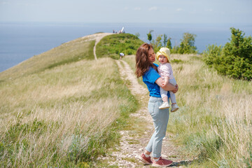 A mother holds a toddler child on top of a mountain with a beautiful view of the mountains and the Volga River, Russia