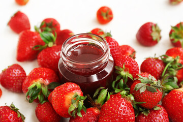 Jar of sweet strawberry jam and fresh berries on light background
